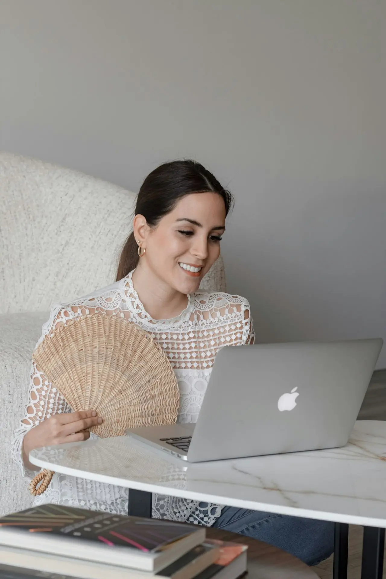 a woman sitting at a table with a laptop and a fan